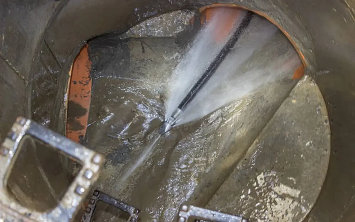 High-pressure hydro jetting nozzle clearing a sewer line from a manhole