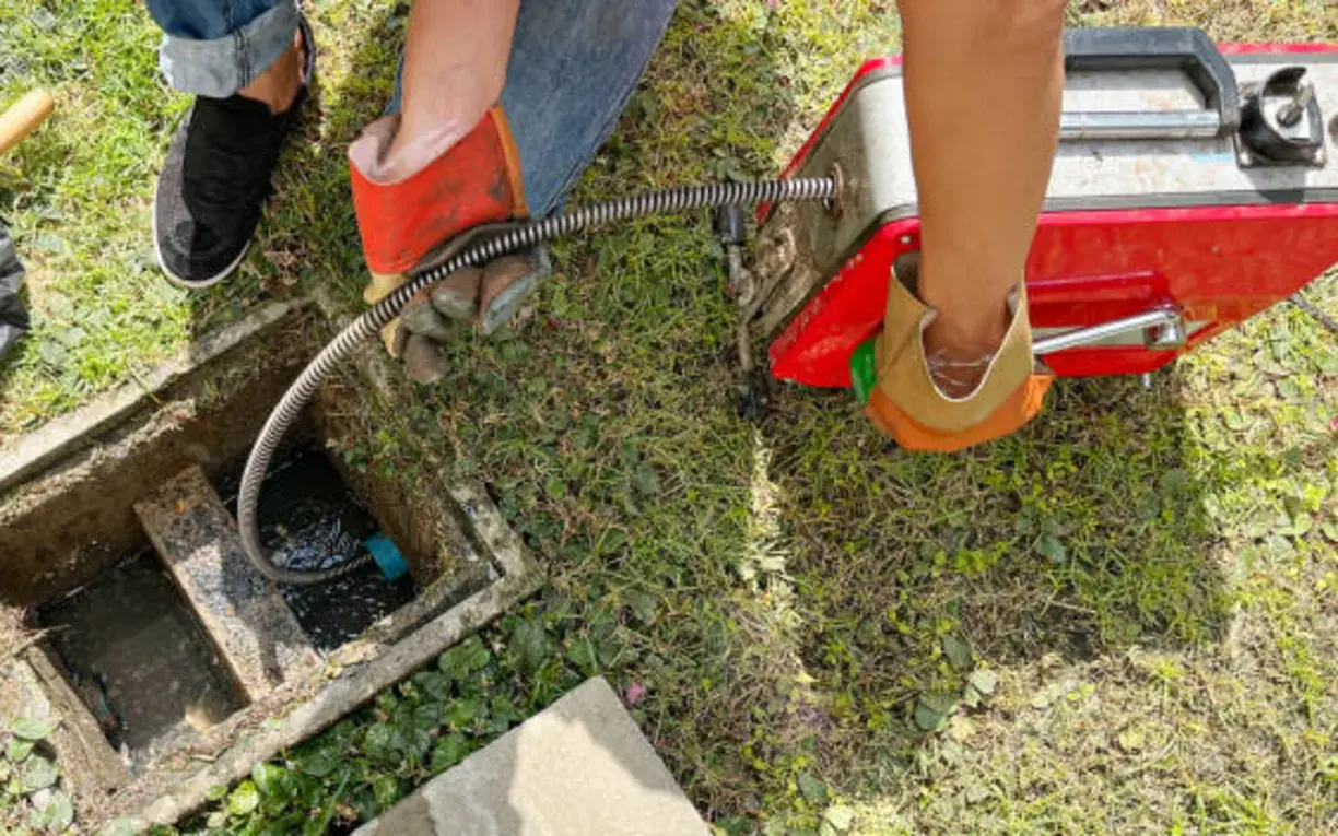 Technician using a motorized cable machine to clear an outdoor sewer cleanout